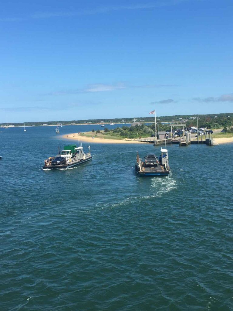 two small car ferries pass by each other travelling between Edgartown and Chappaquiddick on Martha's Vineyard. The Chappaquiddick dock can be seen in the background with a sandy beach on either side