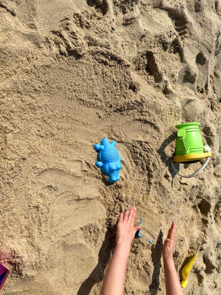 A child's arms reaching towards colorful beach toys on the soft golden South Beach sand