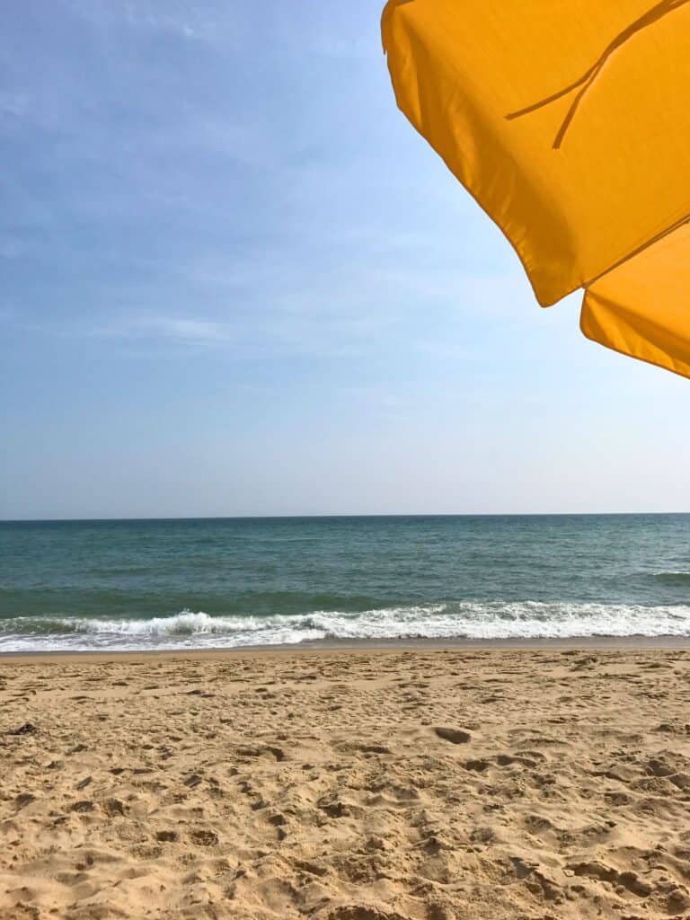 A bright yellow beach umbrella offers a splash of color against the clear blue sky, overlooking the tranquil waves and pristine sandy beach of South Beach on a sunny day